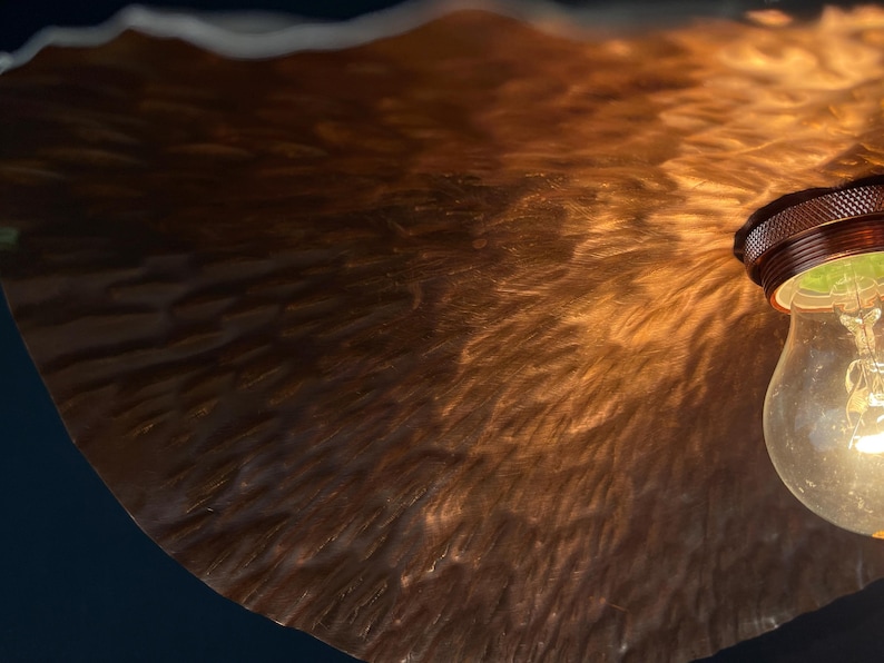 May include: A close-up of a copper-toned lampshade with a textured surface. The lampshade is lit by a light bulb, casting a warm glow.