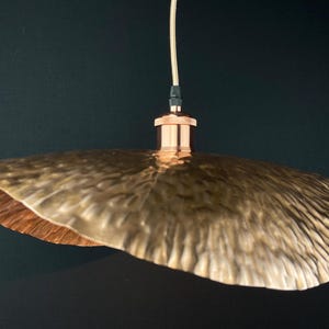 May include: A copper pendant light with a hammered, textured, and slightly wavy shade. The shade is a light gold colour and has a copper finish.