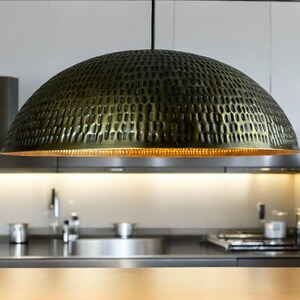 Close-up of handcrafted copper pendant light with hammered perforation pattern and copper interior, suspended above kitchen counter