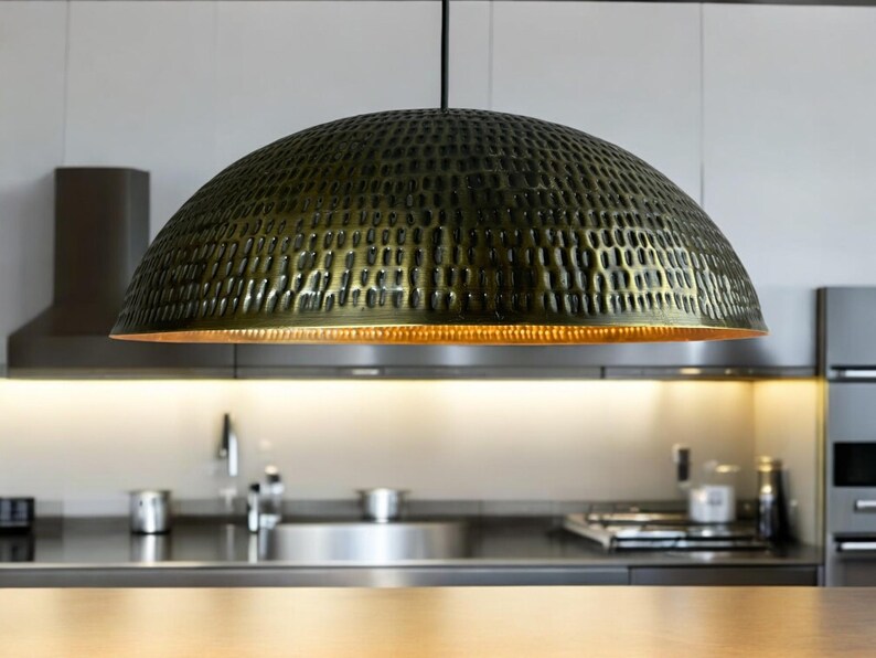 Close-up of handcrafted copper pendant light with hammered perforation pattern and copper interior, suspended above kitchen counter