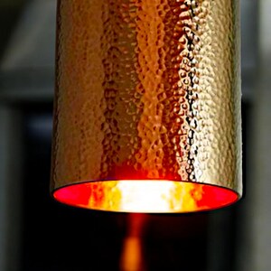 May include: A hammered copper pendant light fixture with a red interior. The light is on and casting a warm glow.