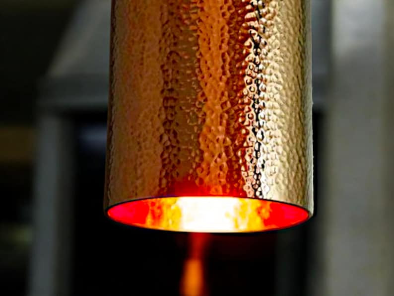May include: A hammered copper pendant light fixture with a red interior. The light is on and casting a warm glow.