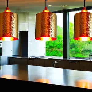 May include: Three gold pendant lights with hammered metal shades hang over a kitchen island. The lights are illuminated, casting a warm glow on the countertop.