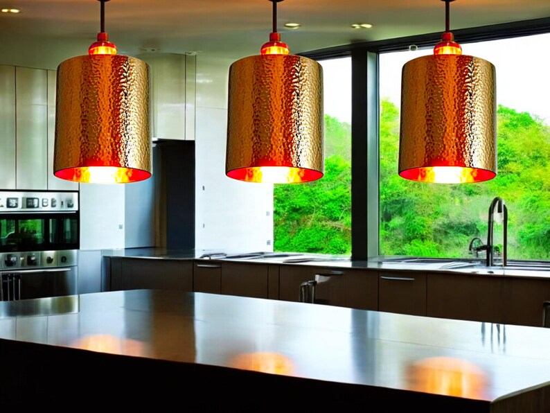 May include: Three gold pendant lights with hammered metal shades hang over a kitchen island. The lights are illuminated, casting a warm glow on the countertop.