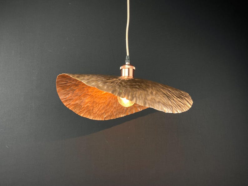 May include: A copper pendant light fitting with a hammered finish and a wide, curved shade. The light is on and casting a warm glow.