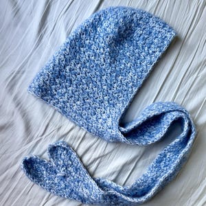 Puede incluir: Una bufanda con capucha de ganchillo azul y blanco con una larga corbata.