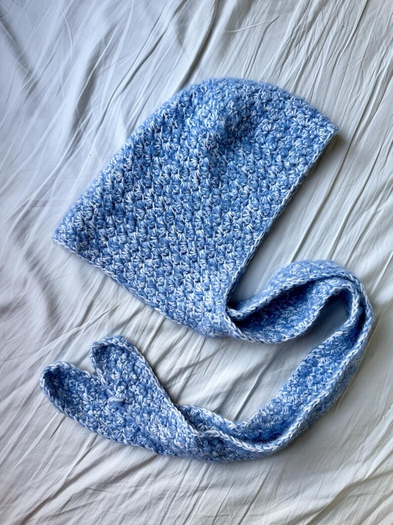 Puede incluir: Una bufanda con capucha de ganchillo azul y blanco con una larga corbata.