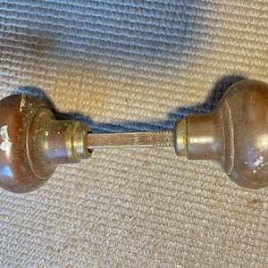 May include: A pair of antique door knobs with a tarnished bronze finish. The knobs are oval-shaped and connected by a metal spindle. The hardware shows signs of wear and age.