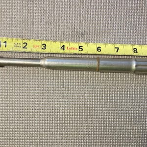 May include: A silver metal tool with a textured handle and a knurled tip, approximately 9 inches long, is positioned next to a yellow measuring tape. The tape shows measurements in inches.