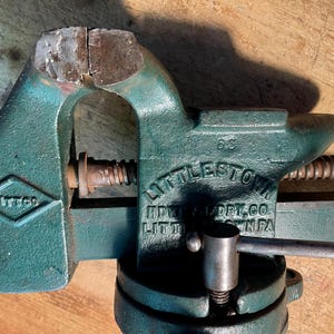 May include: A green metal bench vise with a threaded steel screw and handle. The body features embossed text reading LITTLETOWN HDW & DRY CO LITTLETOWN PA and a diamond-shaped logo with the text LITTECO. The top jaws are metallic and worn.