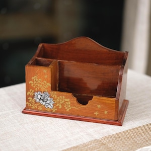 Puede incluir: Organizador de escritorio de madera con múltiples compartimentos. El organizador está teñido de un marrón cálido y presenta un diseño floral con detalles dorados y blancos. La base es de un tono marrón más oscuro. Diseñado para útiles de escritorio.
