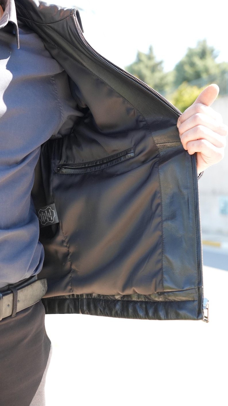 Pu&ograve; includere: Giacca in pelle nera con chiusura a zip e tasca interna. L'interno della giacca &egrave; foderato in tessuto nero. La giacca &egrave; aperta, mostrando la fodera e la tasca. Design classico.