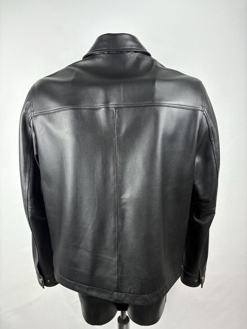 Pu&ograve; includere: Giacca in pelle nera con colletto classico e polsini con bottoni. La giacca ha una vestibilit&agrave; sartoriale e dettagli di cucitura visibili. Il retro della giacca &egrave; visibile, mostrando le cuciture e il design.
