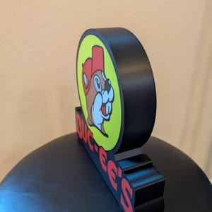 May include: A white ceramic mug with a black handle and the text "But First, Coffee" in a black, handwritten-style font. The mug is on a white surface.