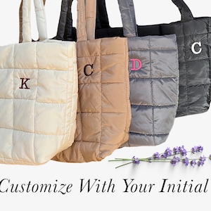 May include: Four quilted tote bags in cream, tan, gray, and black, each with a different embroidered initial. The bags have a square pattern and matching handles. The text "Customize With Your Initial" is at the bottom.