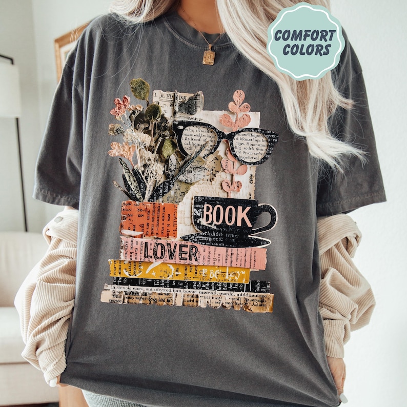 May include: Dark gray t-shirt with a graphic design featuring a stack of books, a coffee cup, and eyeglasses. The word "BOOK" is printed on the cup, and "LOVER" is on the books. The shirt has the words "COMFORT COLORS" in a light blue circle.
