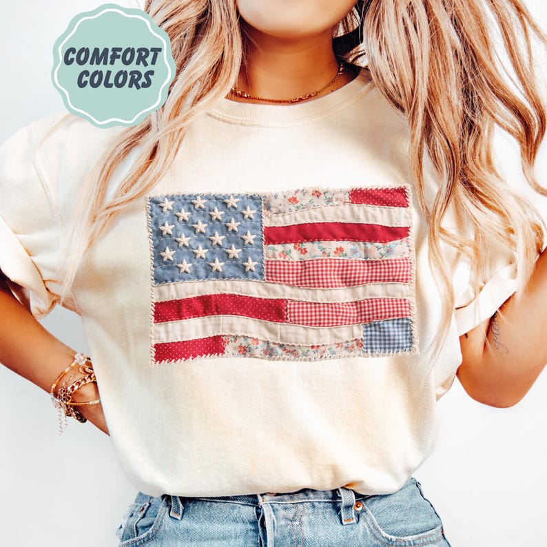 K&ouml;nnte beinhalten: Cremefarbenes Sweatshirt mit einem Patchwork-Design der amerikanischen Flagge. Die Flagge hat blaue Sterne, rote Streifen und Blumen- und Vichy-Muster. Der Text "COMFORT COLORS" befindet sich in einem hellblauen Kreis.