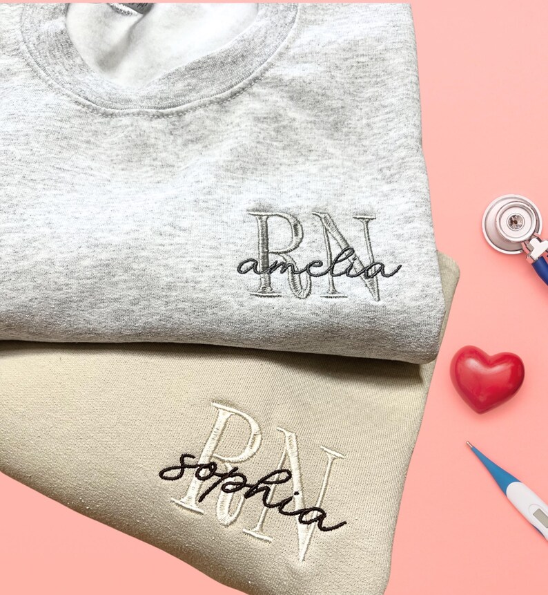 Puede incluir: Dos sudaderas grises y beige con las letras "RN" bordadas. Las sudaderas tambi&eacute;n tienen los nombres "Amelia" y "Sophia" bordados.