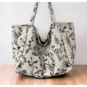 May include: A large, beige tote bag with black floral print. The bag has two long handles and a wide opening.