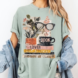 May include: A light green t-shirt featuring a collage design for book lovers. The design includes a stack of books, a coffee cup, eyeglasses, and floral elements. The word "BOOK" is printed on the cup, and "LOVER" is printed on the books.