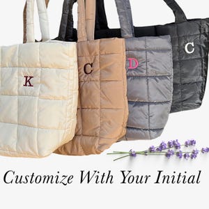 May include: Four quilted tote bags in cream, tan, gray, and black, each with a different initial embroidered on the front. The bags have matching handles and a square quilted pattern. The text "Customize With Your Initial" is at the bottom.