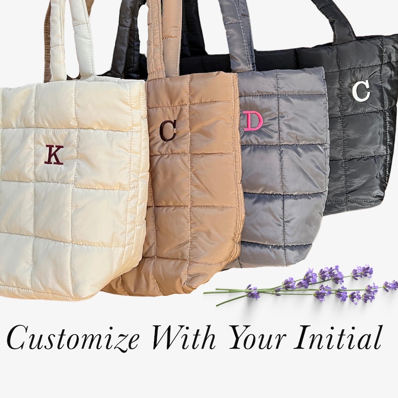May include: Four quilted tote bags in cream, tan, gray, and black, each with a different initial embroidered on the front. The bags have matching handles and a square quilted pattern. The text "Customize With Your Initial" is at the bottom.