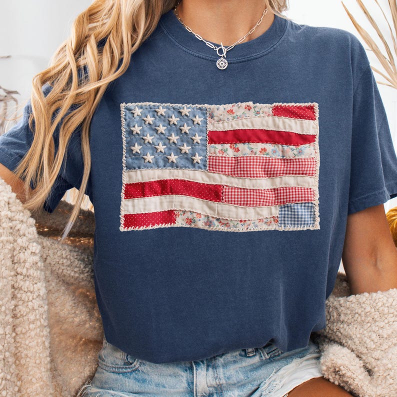 K&ouml;nnte beinhalten: Marineblaues T-Shirt mit einem Patchwork-Design der amerikanischen Flagge. Die Flagge verwendet rote, wei&szlig;e und blaue Stoffe mit Blumen- und Vichy-Mustern. Das T-Shirt hat einen Rundhalsausschnitt und kurze &Auml;rmel.
