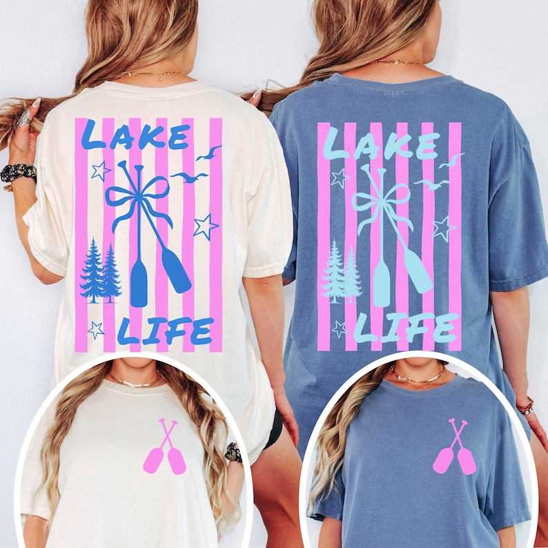 May include: Two t-shirts, one cream and one blue, feature a "Lake Life" design. The design includes pink vertical stripes, blue oars, trees, stars, and the text "Lake Life". A smaller design of crossed oars is on the front.