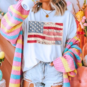 K&ouml;nnte beinhalten: Wei&szlig;es T-Shirt mit einem Patchwork-Design der amerikanischen Flagge. Die Flagge verwendet gemusterte Stoffe in Rot, Wei&szlig; und Blau. Die Person tr&auml;gt eine farbenfrohe gestreifte Strickjacke und Jeansshorts.