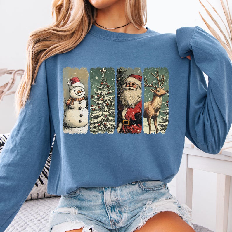 May include: A blue long-sleeve sweatshirt featuring a festive Christmas design. The design includes a snowman, Christmas tree, Santa Claus, and a reindeer, all within rectangular frames. The illustrations are in a vintage style, evoking a nostalgic holiday feel.