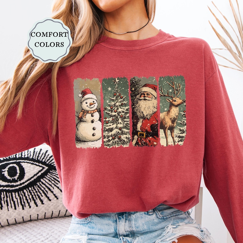 May include: A maroon Comfort Colors sweatshirt featuring a Christmas-themed graphic. The graphic includes a snowman, Christmas tree, Santa Claus, and a reindeer, each in a vertical rectangular panel. The sweatshirt has a crew neck.