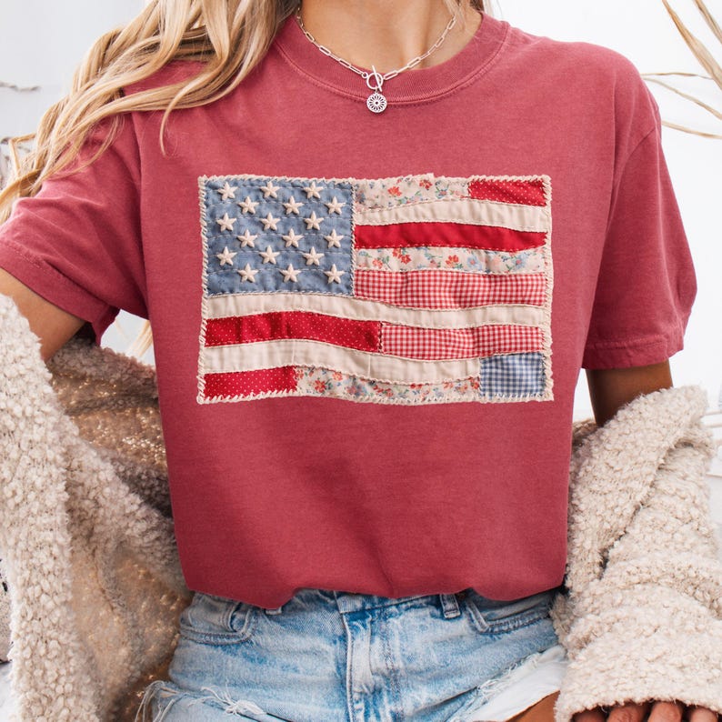 K&ouml;nnte beinhalten: Ein weinrotes T-Shirt mit einem Patchwork-Design der amerikanischen Flagge. Die Flagge hat blaue Sterne, rot-wei&szlig;e Streifen und Blumen- und Vichy-Muster. Das T-Shirt ist aus weichem Material.