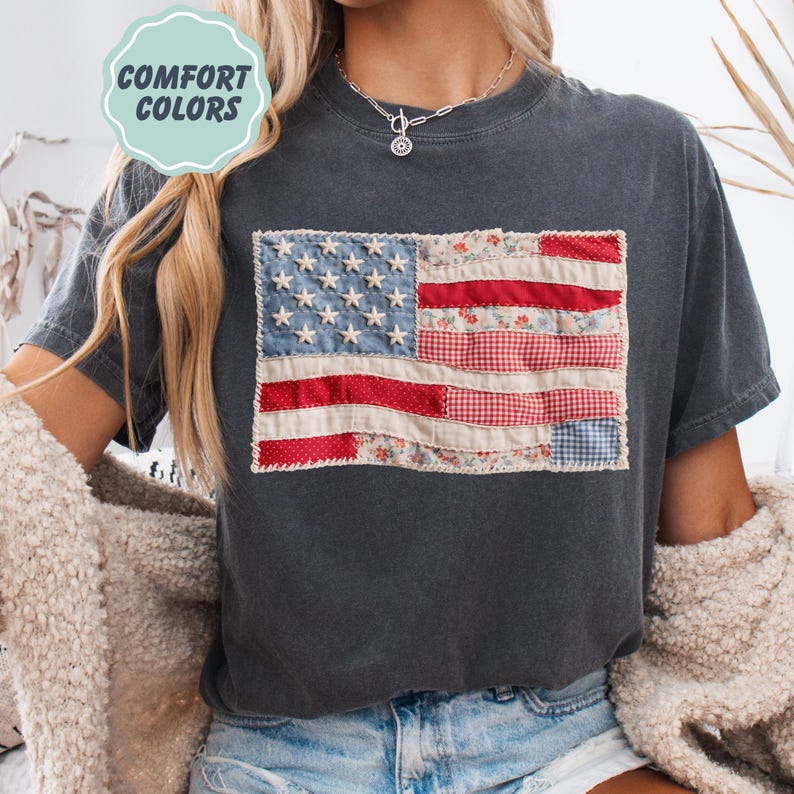 K&ouml;nnte beinhalten: Dunkelgraues T-Shirt mit einem Patchwork-Design der amerikanischen Flagge. Die Flagge verwendet rot-, wei&szlig;- und blau gemusterte Stoffe, darunter Blumen- und Vichymuster. Das T-Shirt hat den Text "COMFORT COLORS" in einem hellgr&uuml;nen Kreis.