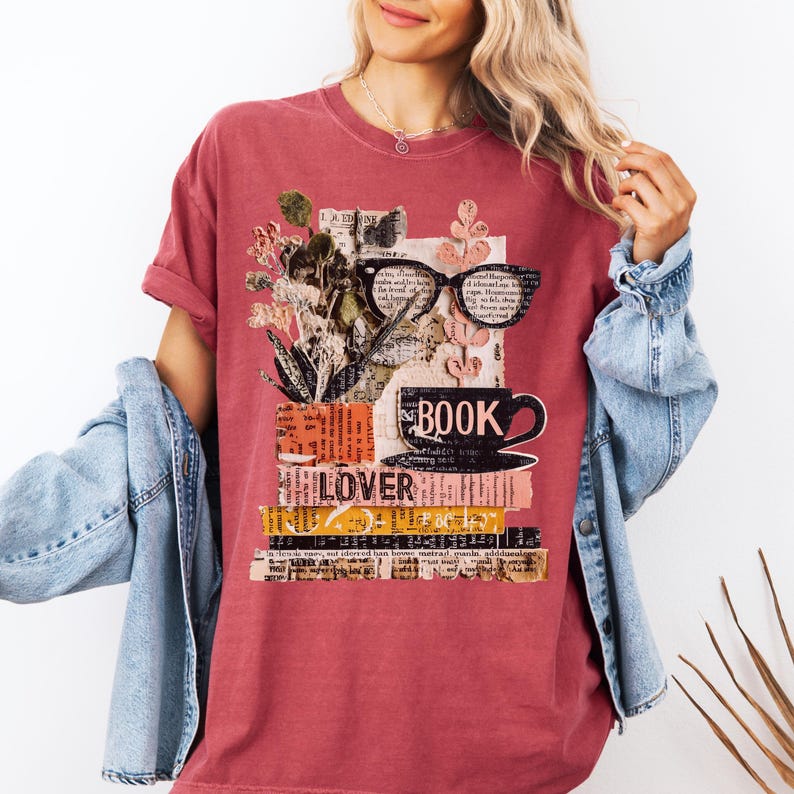 May include: A maroon t-shirt featuring a collage design for book lovers. The design includes a stack of books, eyeglasses, a coffee cup, and the words "BOOK LOVER". The shirt has short sleeves and a relaxed fit.