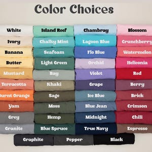 May include: A color chart displaying folded t-shirts in various shades. The text labels include White, Ivory, Banana, Butter, Mustard, Terracotta, Burnt Orange, Yam, Grey, Granite, Graphite, Island Reef, Chalky Mint, Seafoam, Light Green, Bay, Khaki, Sage, Moss, Hemp, Blue Spruce, Pepper, Chambray, Lagoon Blue, Flo Blue, Orchid, Violet, Grape, Ice Blue, Blue Jean, Midnight, True Navy, Blossom, Crunchberry, Watermelon, Heliconia, Red, Berry, Brick, Crimson, Chili, Espresso, and Black.