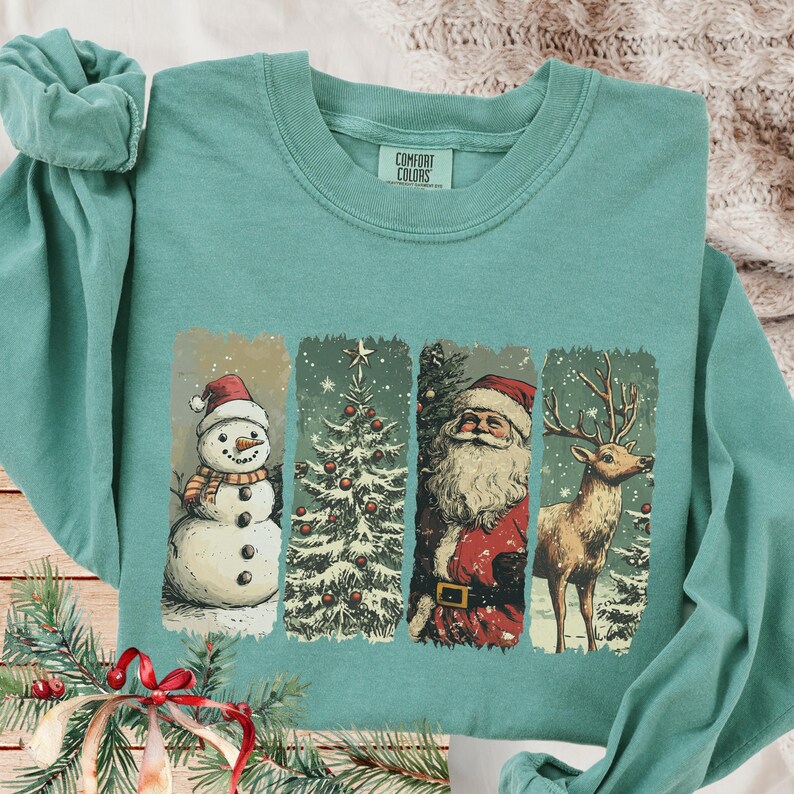 May include: Teal long-sleeve sweatshirt featuring a festive Christmas design. The design includes a snowman, Christmas tree, Santa Claus, and a reindeer. The brand name "Comfort Colors" is printed on the upper right of the sweatshirt.