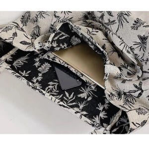 May include: A black and white floral print tote bag with a laptop and a phone inside. The bag is made of a canvas material and has a zipper closure.