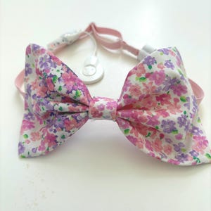 May include: A pink floral bow tie with a white button and a pink elastic band.