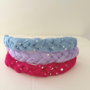 以下が含まれることがあります： 青、紫、ピンクの3色の編み込みヘアバンド。各ヘアバンドはシアー生地で作られ、銀色の星と月のアクセントで飾られています。ヘアバンドは互いの上に積み重ねられています。