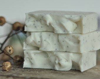May include: Three bars of white soap with black poppy seeds. The soap is stacked on top of each other.