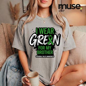 Puede incluir: Camiseta gris con el texto "I WEAR GREEN FOR MY BROTHER" en una fuente llamativa, con un lazo verde. La camiseta también incluye el texto "CEREBRAL PALSY AWARENESS".