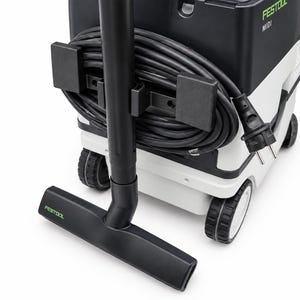 Può includere: Un aspiratore mobile Festool MIDI con corpo nero e bianco, tubo di aspirazione nero, bocchetta per pavimenti nera con marchio verde e cavo di alimentazione nero avvolto sul retro dell'unità, montato su quattro ruote.