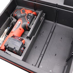 Puede incluir: Un cajón de almacenamiento de herramientas de plástico negro con un inserto de espuma personalizado. El cajón contiene una sierra de calar inalámbrica roja y negra, una batería de iones de litio y varias hojas de sierra de metal.
