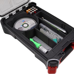 Può includere: Una valigetta rigida rettangolare nera con maniglia e chiusura rosse, coperchio aperto e scomparti interni. La valigetta contiene un disco circolare, un piccolo utensile verde, diverse batterie e vari contenitori in plastica trasparente.