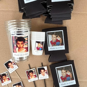 Peut inclure: Ensemble de fournitures de f&ecirc;te avec une photo d'enfant et le texte "Made in 1987". Comprend des gobelets en plastique transparents, des petits gobelets blancs, des refroidisseurs de canettes noirs et des d&eacute;corations photo. Sur une surface brune.