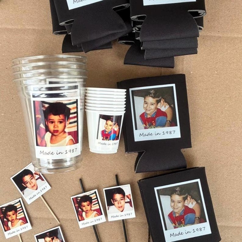 Peut inclure: Ensemble de fournitures de f&ecirc;te avec une photo d'enfant et le texte "Made in 1987". Comprend des gobelets en plastique transparents, des petits gobelets blancs, des refroidisseurs de canettes noirs et des d&eacute;corations photo. Sur une surface brune.