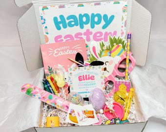 May include: An Easter-themed gift box filled with colorful toys and stationery. Includes a card with "Happy Easter" in teal and pink, a pink notebook, a bunny mask, pencils, and a variety of other Easter-themed items.