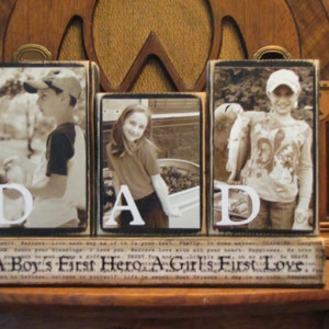 K&ouml;nnte beinhalten: Drei Holzbl&ouml;cke mit dem Wort "DAD" in wei&szlig;en Buchstaben. Jeder Block zeigt ein Schwarzwei&szlig;foto eines Kindes. Der untere Block hat den Text "A Boy's First Hero & A Girl's First Love".