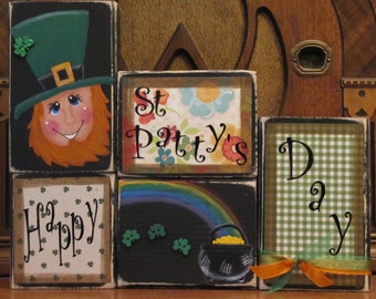 May include: A set of five wooden blocks with a St. Patrick's Day theme. The blocks are painted with a leprechaun, a rainbow, shamrocks, a pot of gold, the words "Happy", "St. Patty's", and "Day".