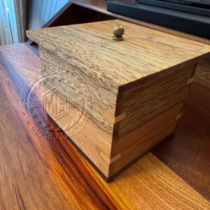 May include: A wooden box with a hinged lid and a brass knob. The box is made of different types of wood, creating a unique pattern.